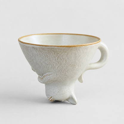 Ivory cat-shaped ceramic cup with the opening facing up and a curved tail handle
